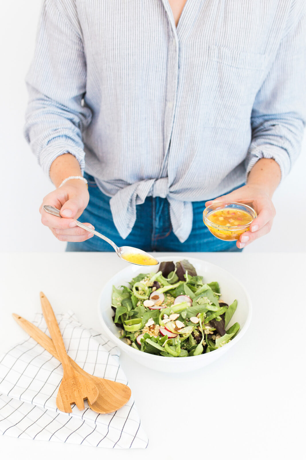 person drizzling dressing on to a salad in a bowl