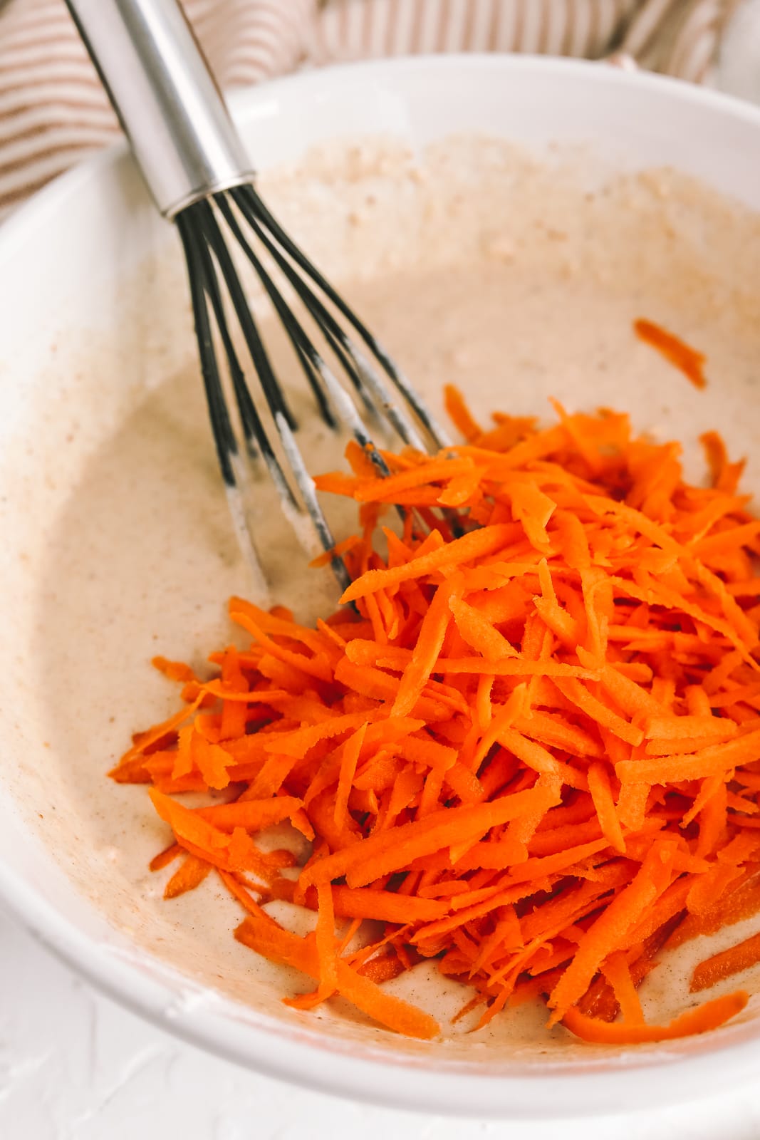 a bowl with pancake batter and carrots being mixed in