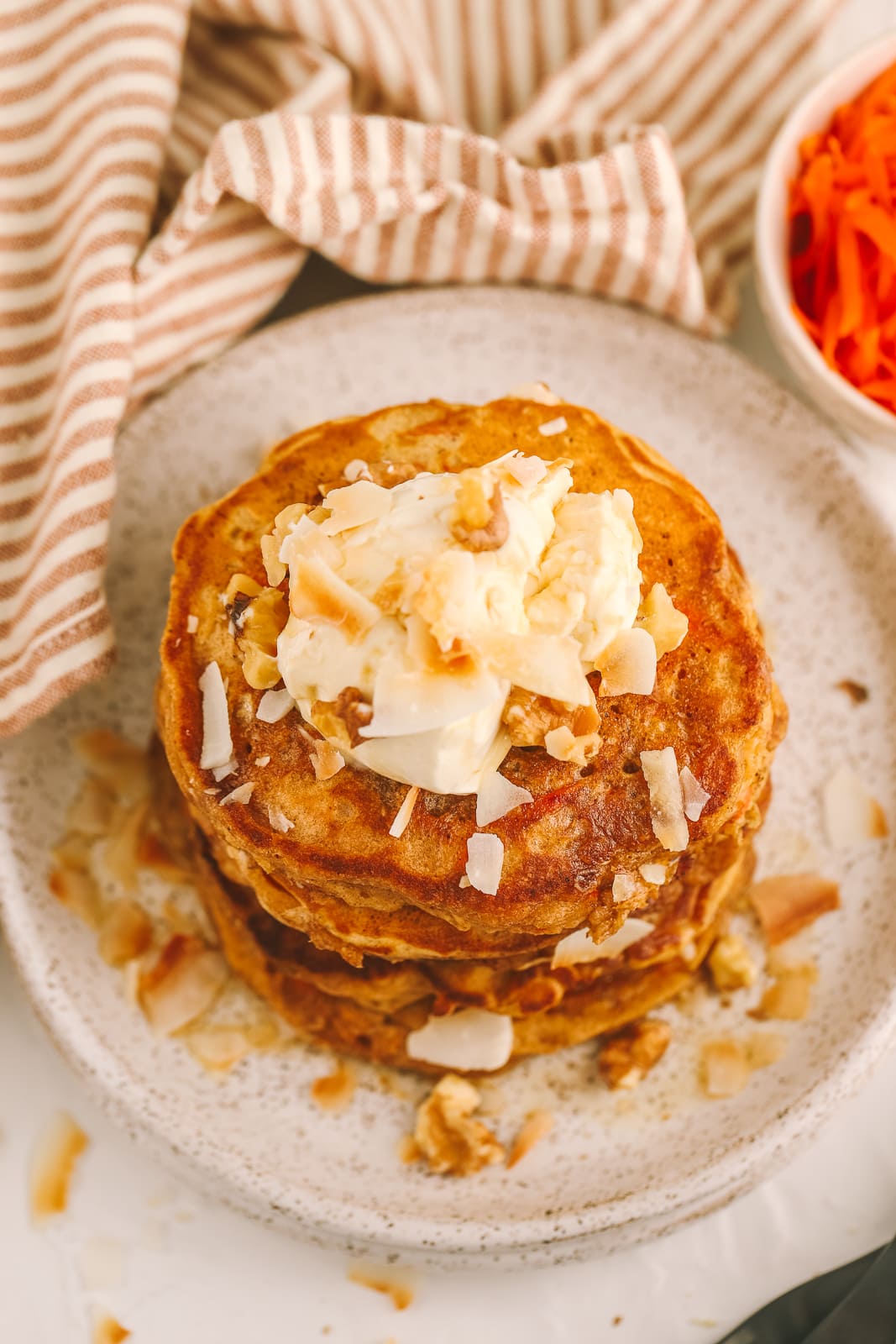 overhead photo of carrot cake pancakes topped with cream cheese, coconut and walnuts
