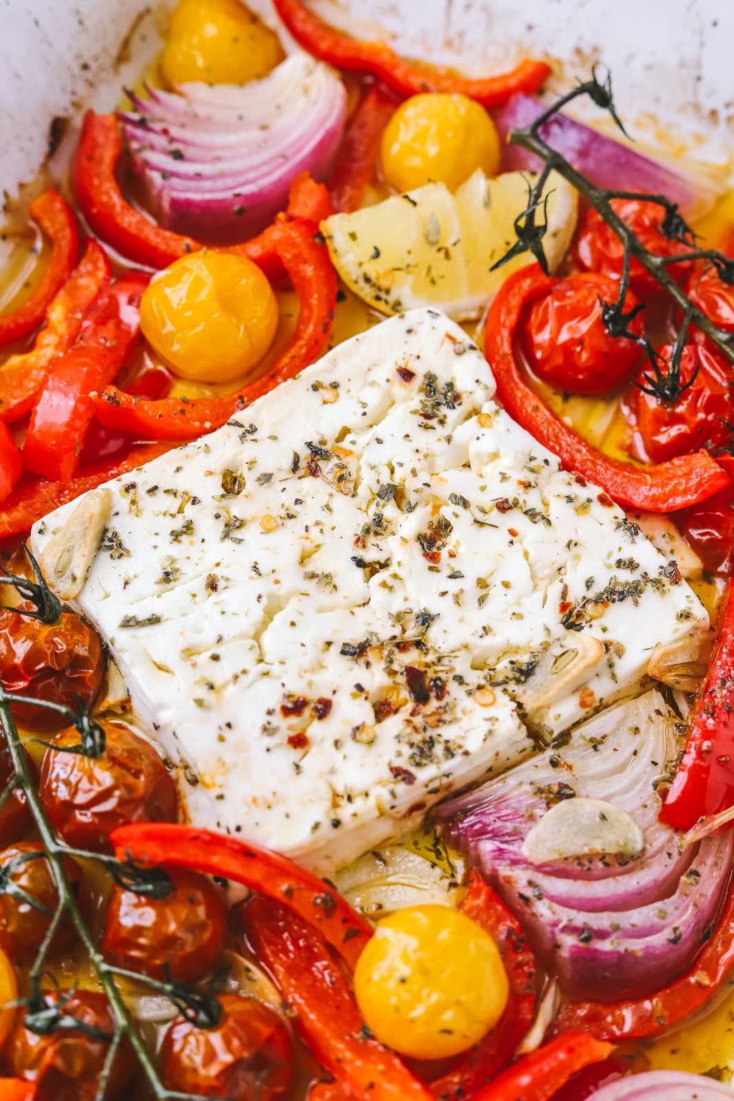 side angle of baked feta in a pan with summer vegetables