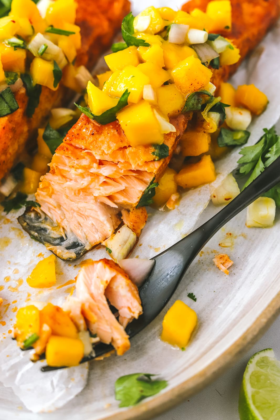 bite of chili lime baked salmon topped with mango salsa on a plate