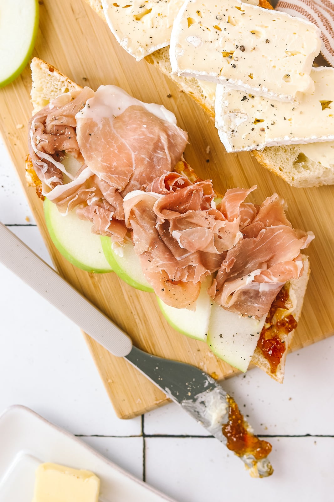 prosciutto and apple on a baguette being made on a cutting board