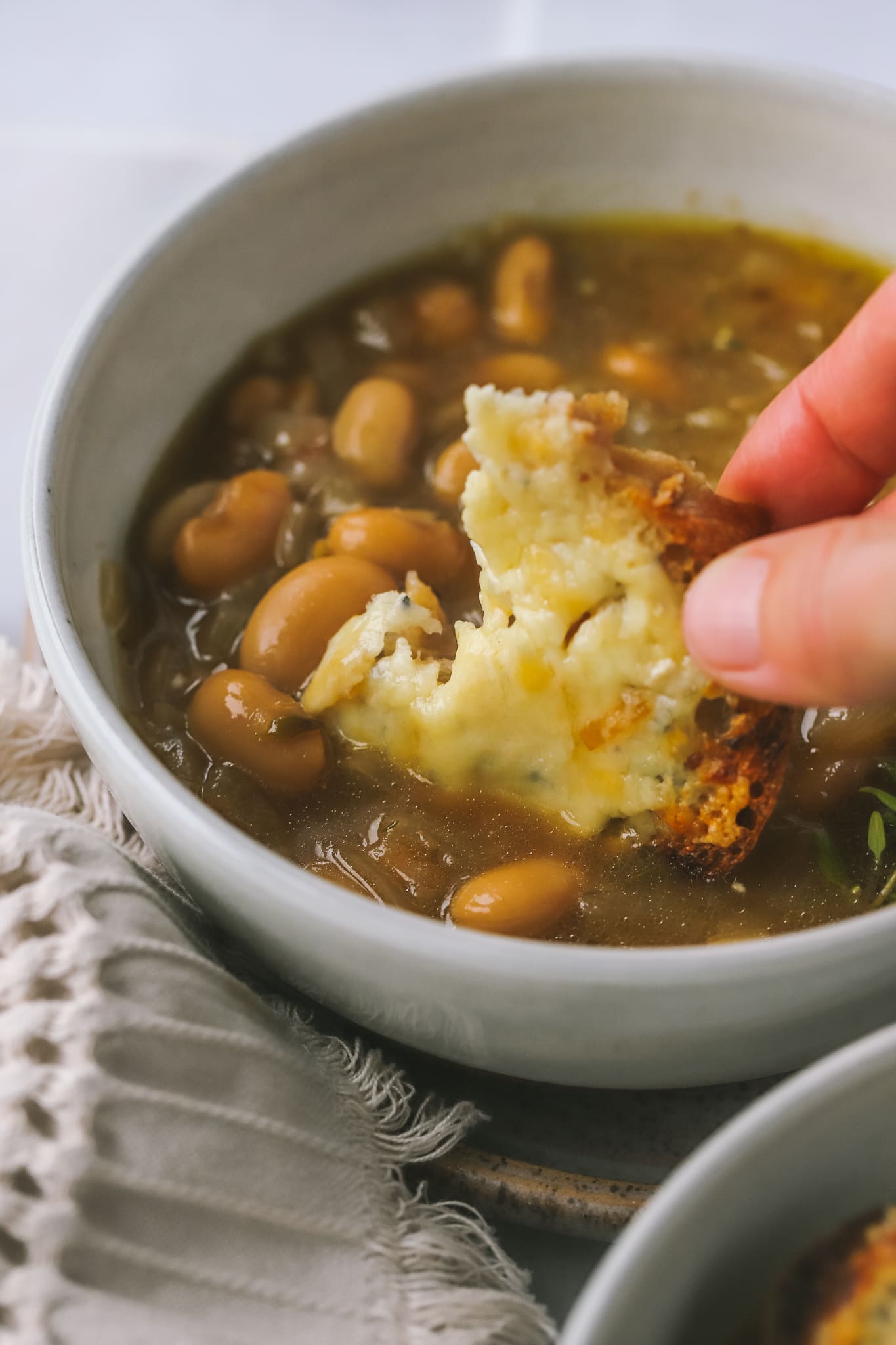 hand dipping cheesy toast in french onion bean soup