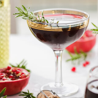 pomegranate cocktail in a coupe glass garnished with rosemary sprig