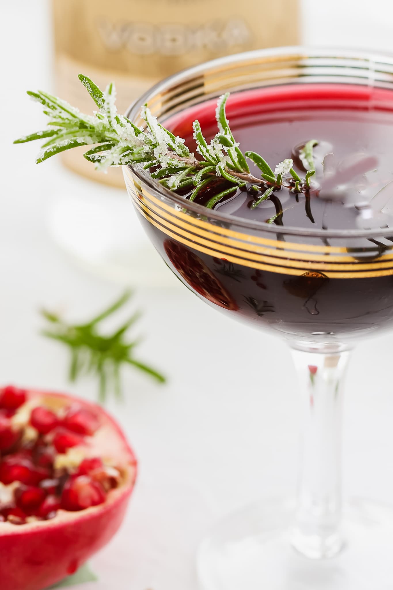 closeup of a sugared rosemary sprig in pomegranate vodka cocktails