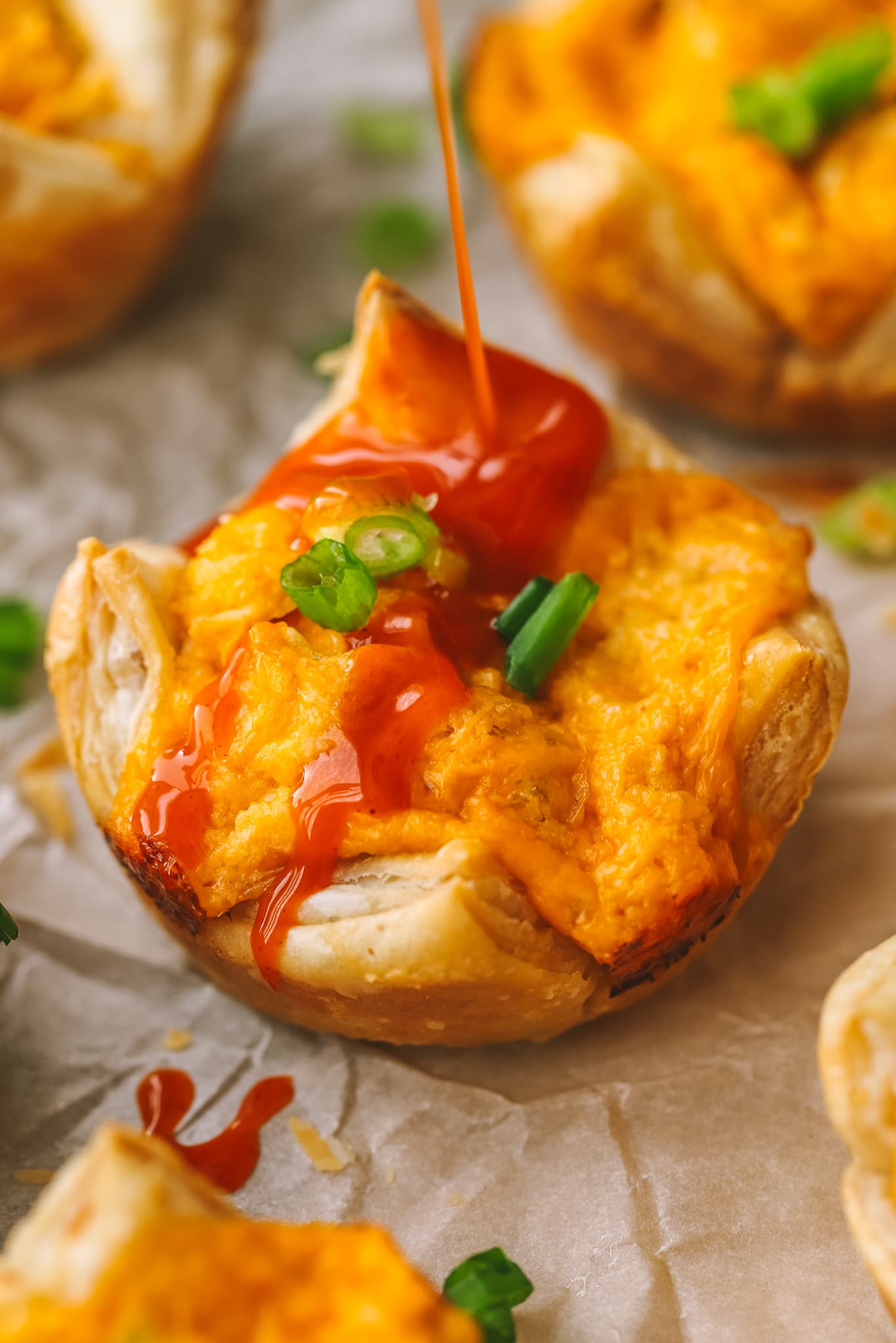 buffalo sauce being drizzled onto a puff pastry chicken bite