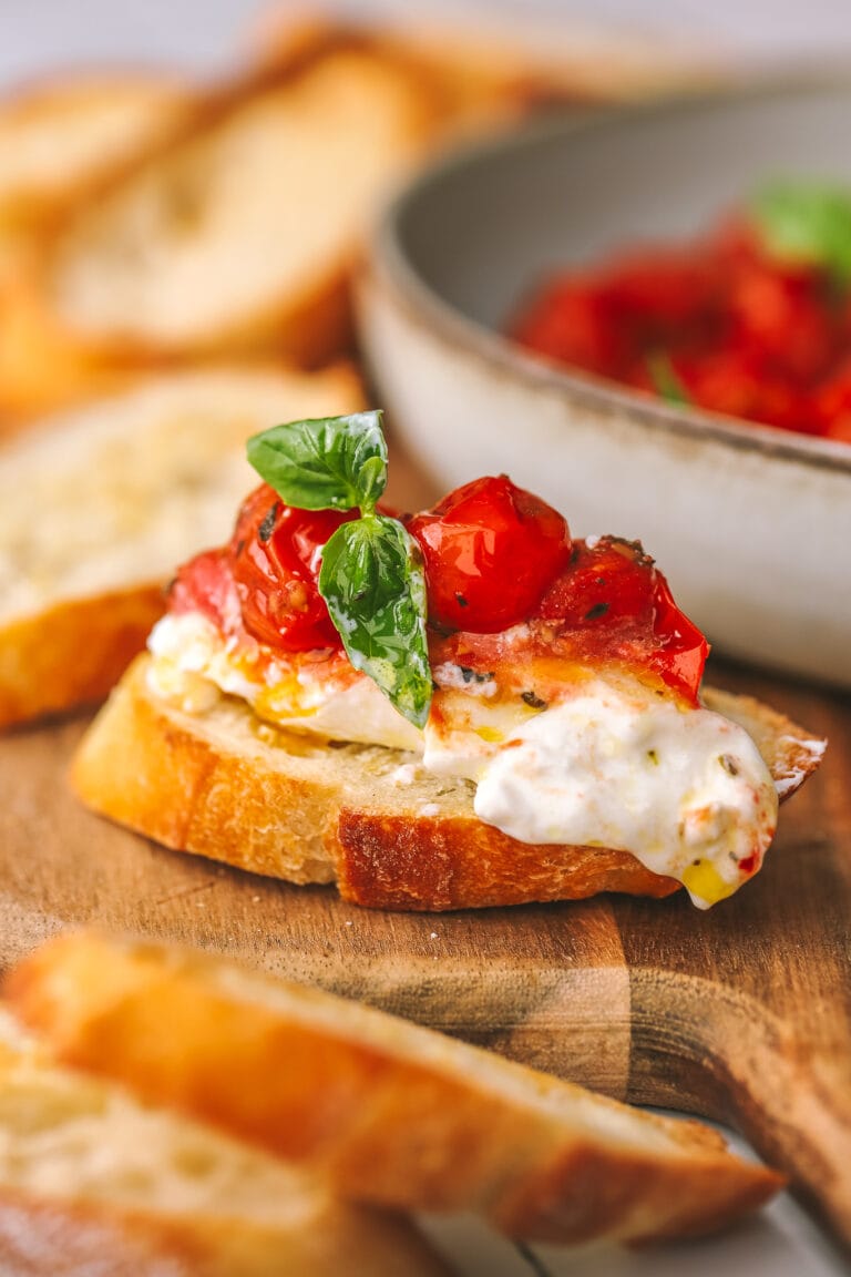side angle of burrata on bread topped with roasted tomatoes