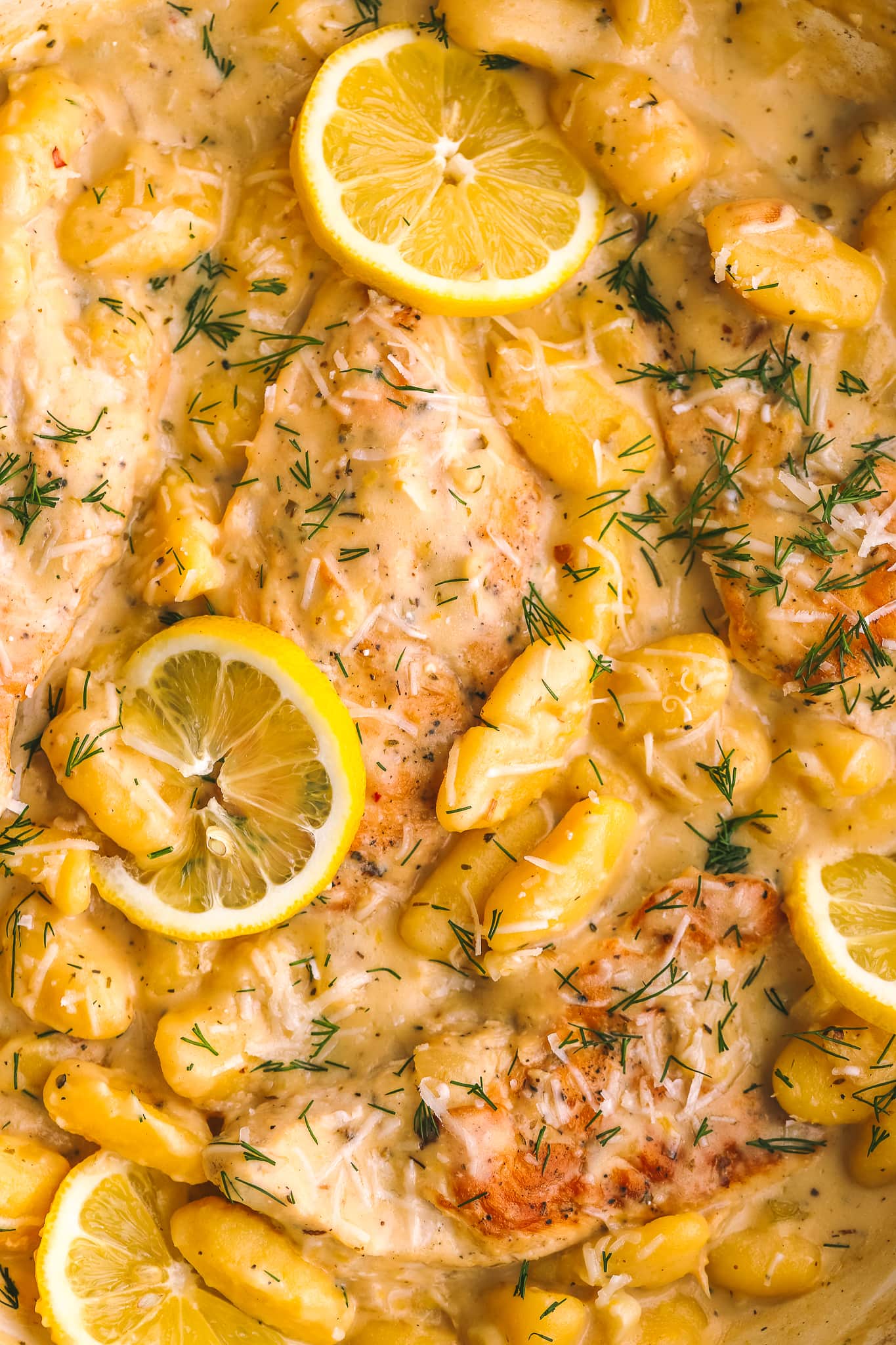 closeup of cooked chicken, gnocchi and lemon in a large pan