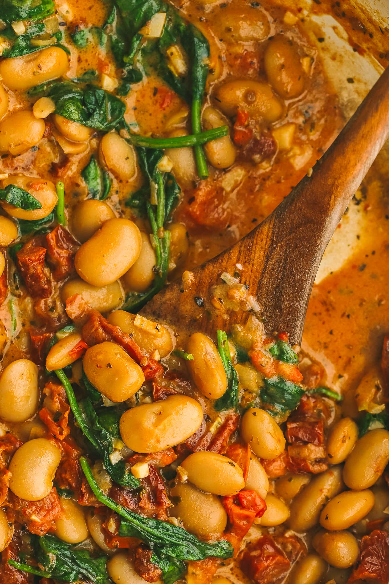 wooden spoon in a pot of cooked butter beans and sundried tomato sauce