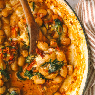 wooden spoon in a pot of cooked butter beans and sundried tomato sauce