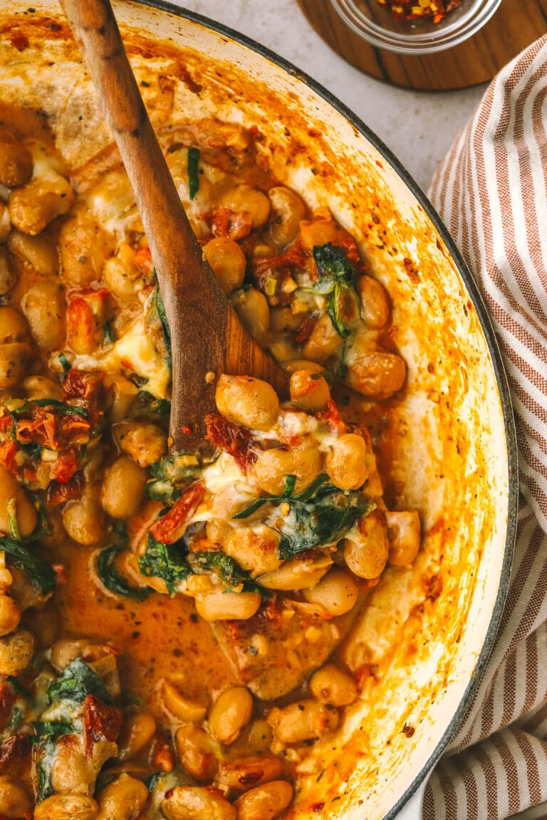 wooden spoon in a pot of cooked butter beans and sundried tomato sauce