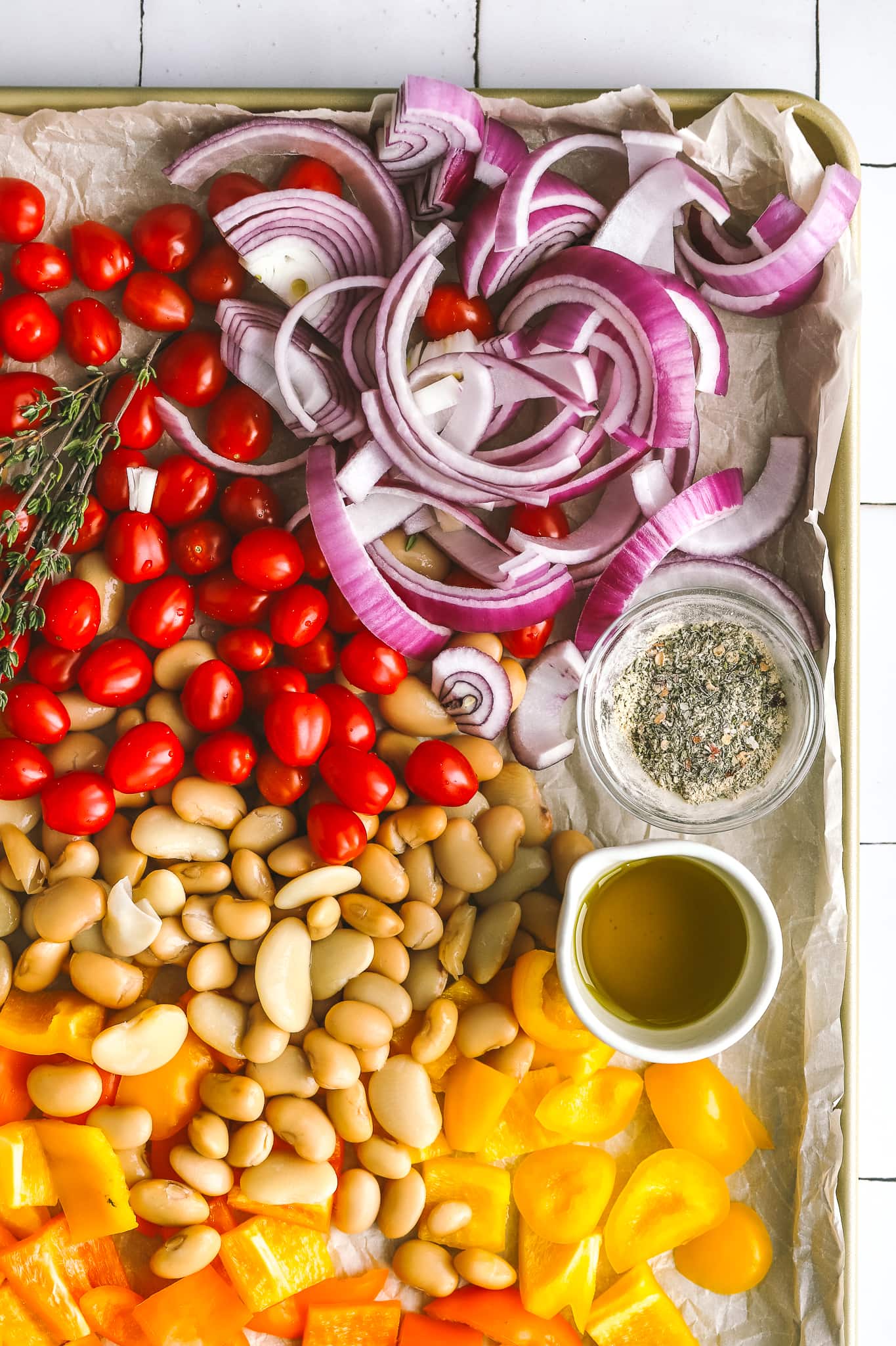 sliced onions, baby tomatoes, beans, peppers on a sheet pan