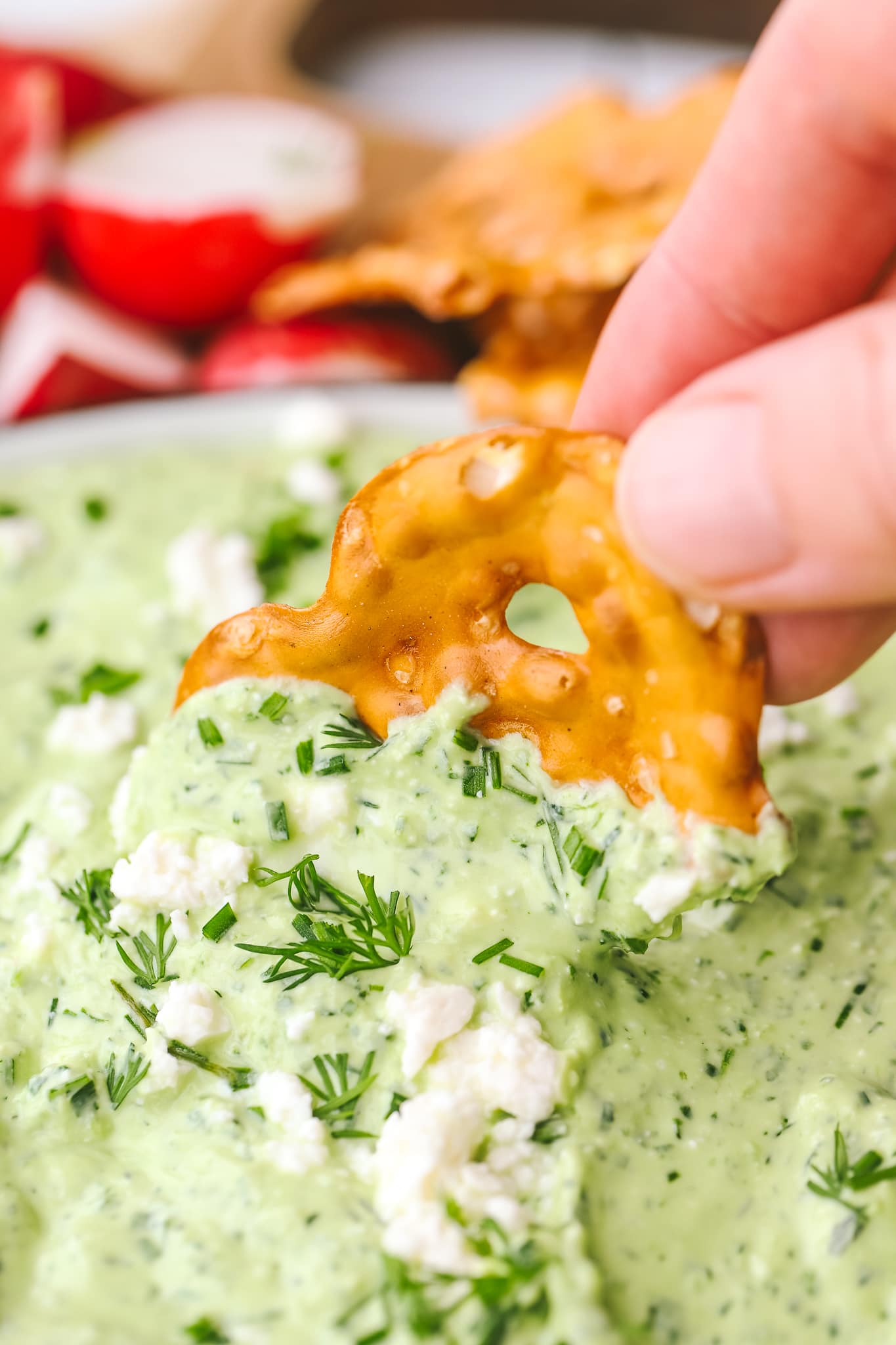 hand holding a pretzel cracker dipped in green goddess whipped feta