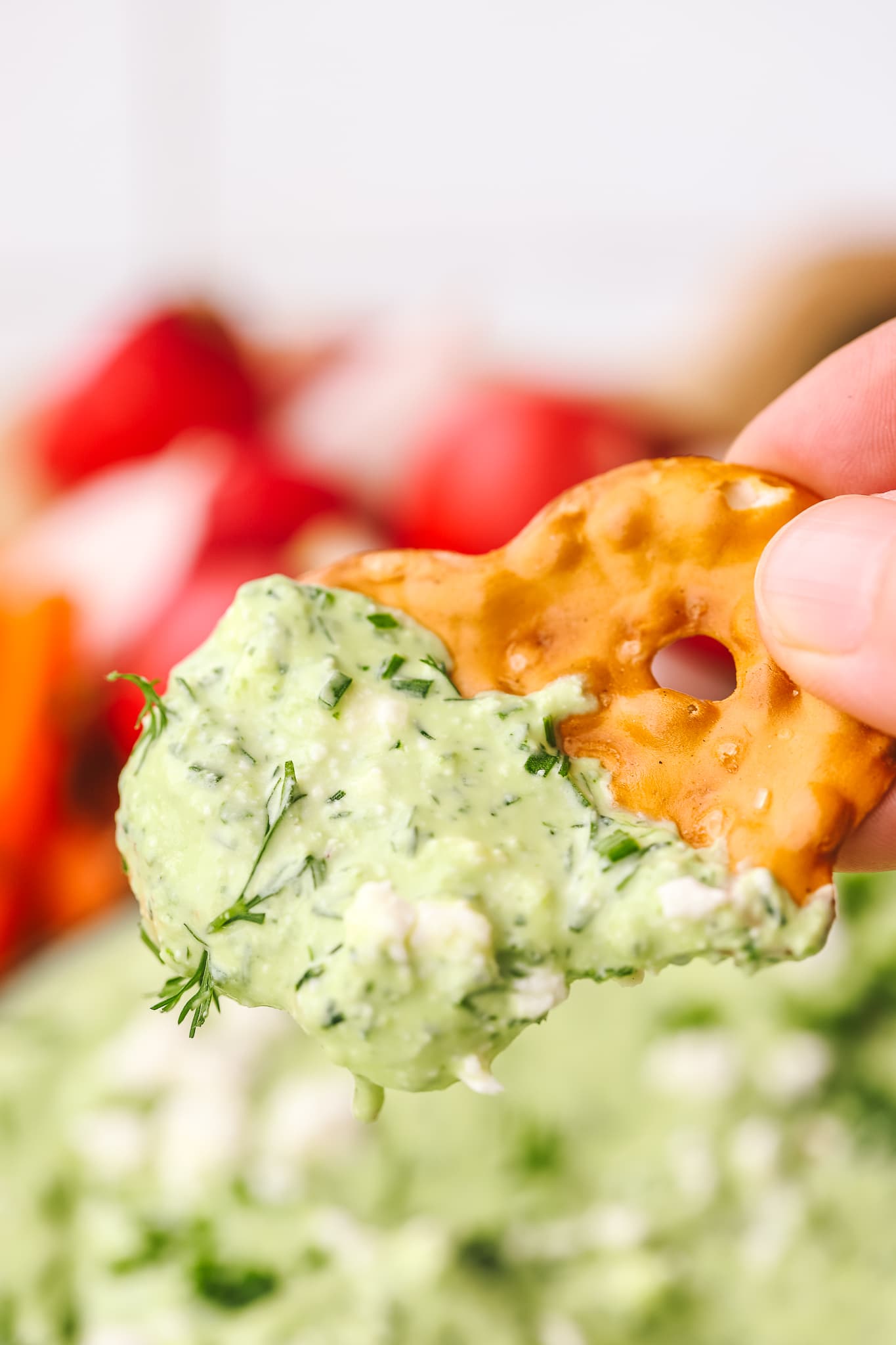 hand holding a pretzel cracker dipped in green goddess whipped feta