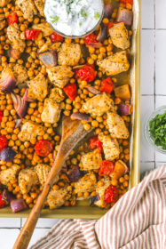 serving spoon in roasted chicken with chickpeas and tomatoes on a sheet pan