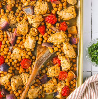 serving spoon in roasted chicken with chickpeas and tomatoes on a sheet pan