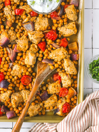 serving spoon in roasted chicken with chickpeas and tomatoes on a sheet pan