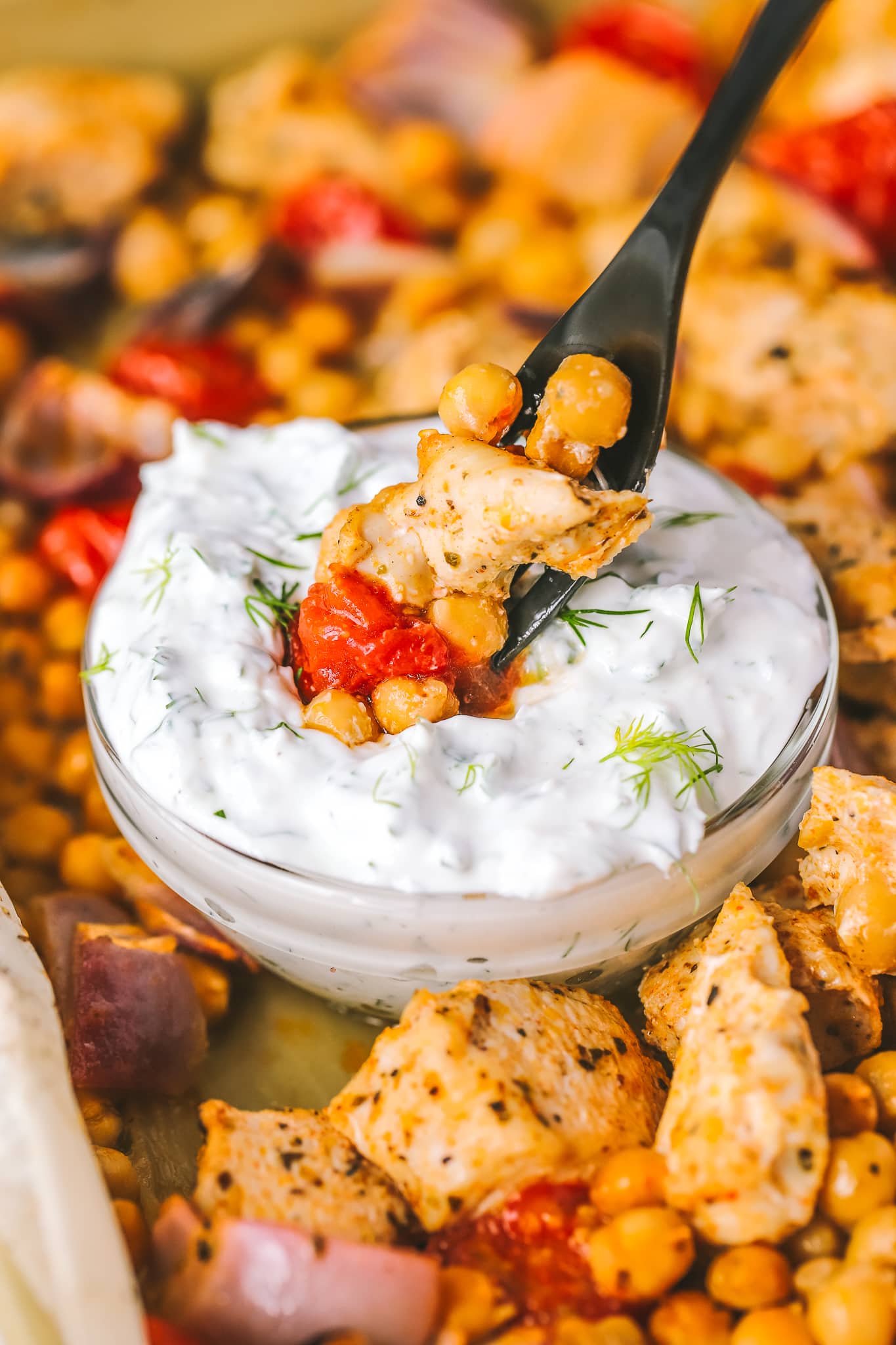 forkful of chickpeas, chicken and tomatoes dipping into herby yogurt sauce