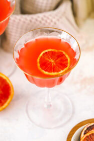 angled shot of a glass with blood orange martini and blood orange garnish