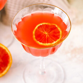 angled shot of a glass with blood orange martini and blood orange garnish