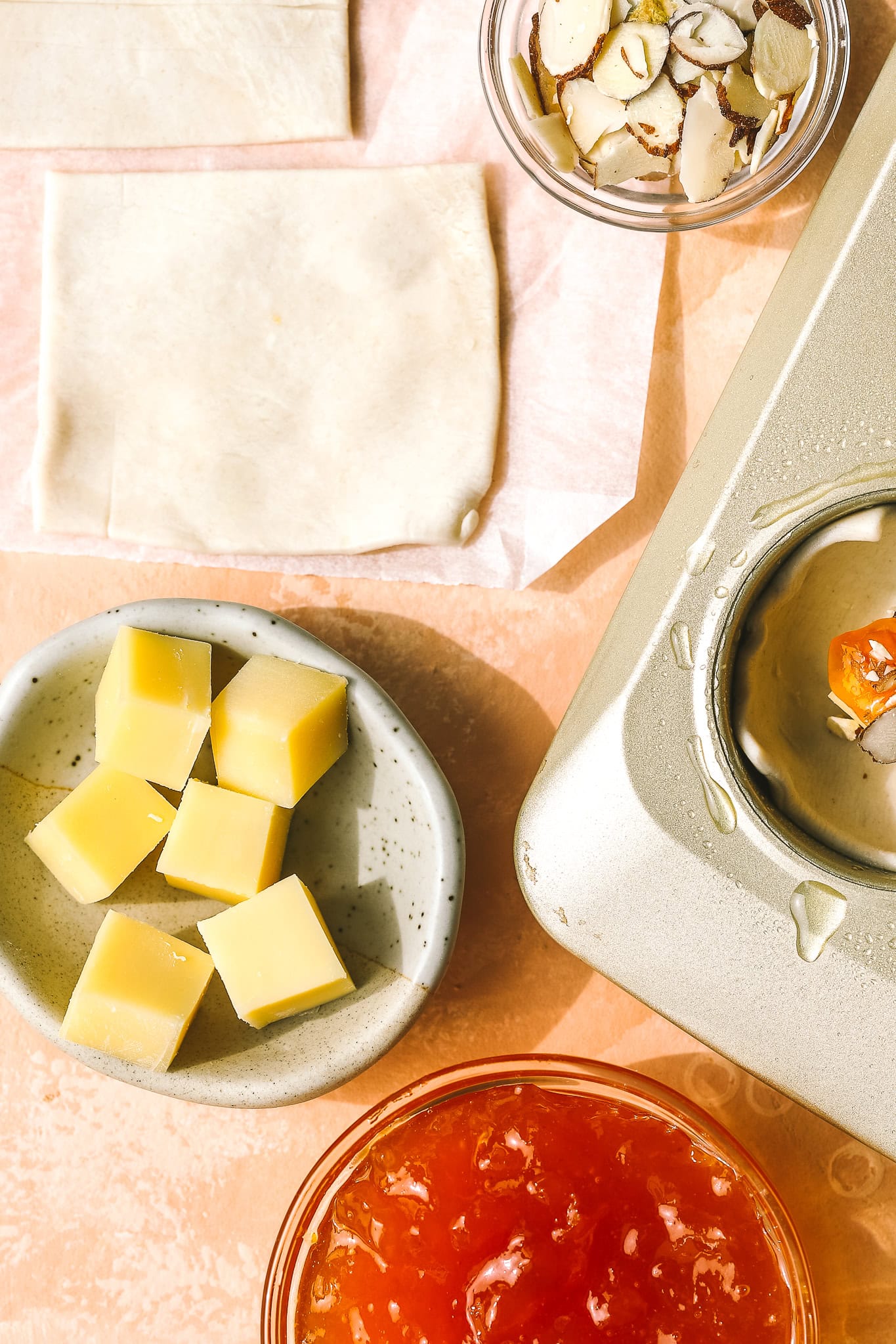 cubes of gruyere cheese, puff pastry squares and apricot jam in a bowl