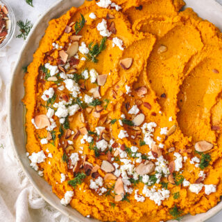 carrot hummus spread in a low bowl with toppings