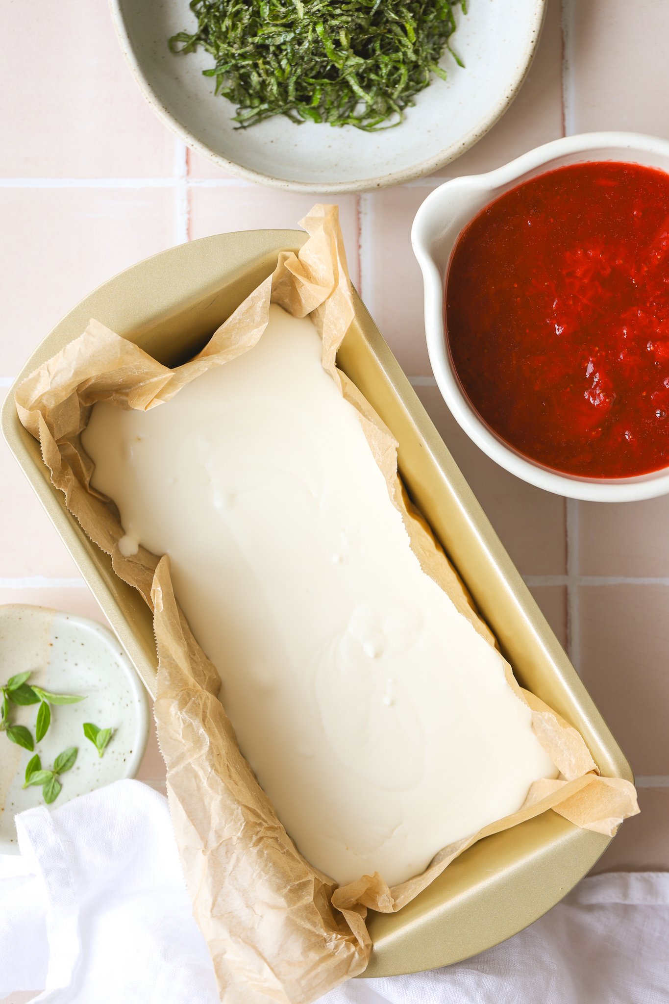 no churn ice cream base in a loaf pan, basil in a bowl and strawberry puree in a bowl