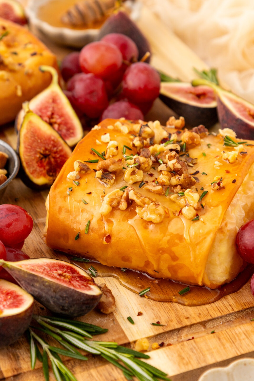 close up of baked feta on a serving board with grapes and figs