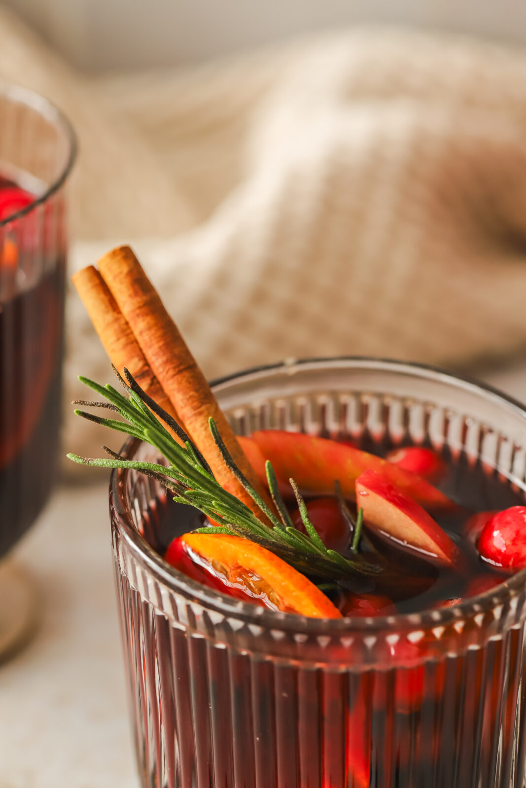 close up of cinnamon stick and rosemary garnish in a glass of red sangria