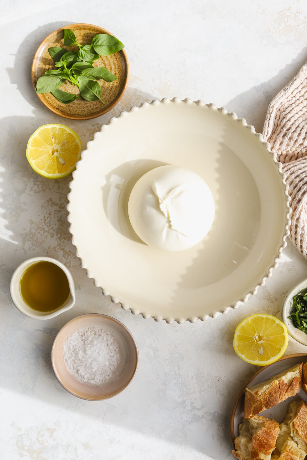burrata ball in a bowl, fresh basil leaves, olive oil, salt in a bowl, lemon slices