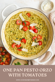 pesto orzo in a braiser topped with parmesan cheese and fresh tomatoes