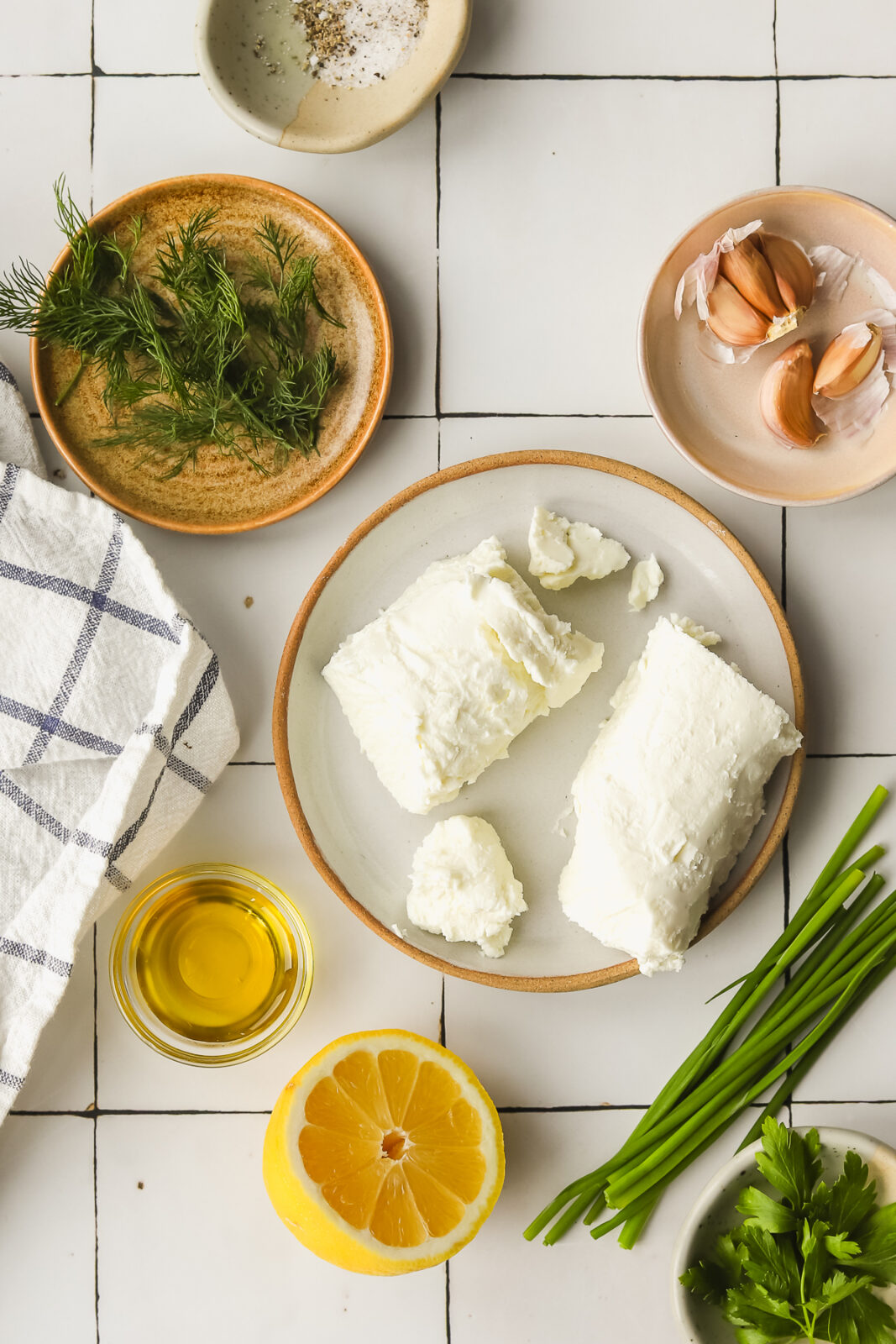 goat cheese on a plate, fresh herbs in bowls, olive oil in a bowl