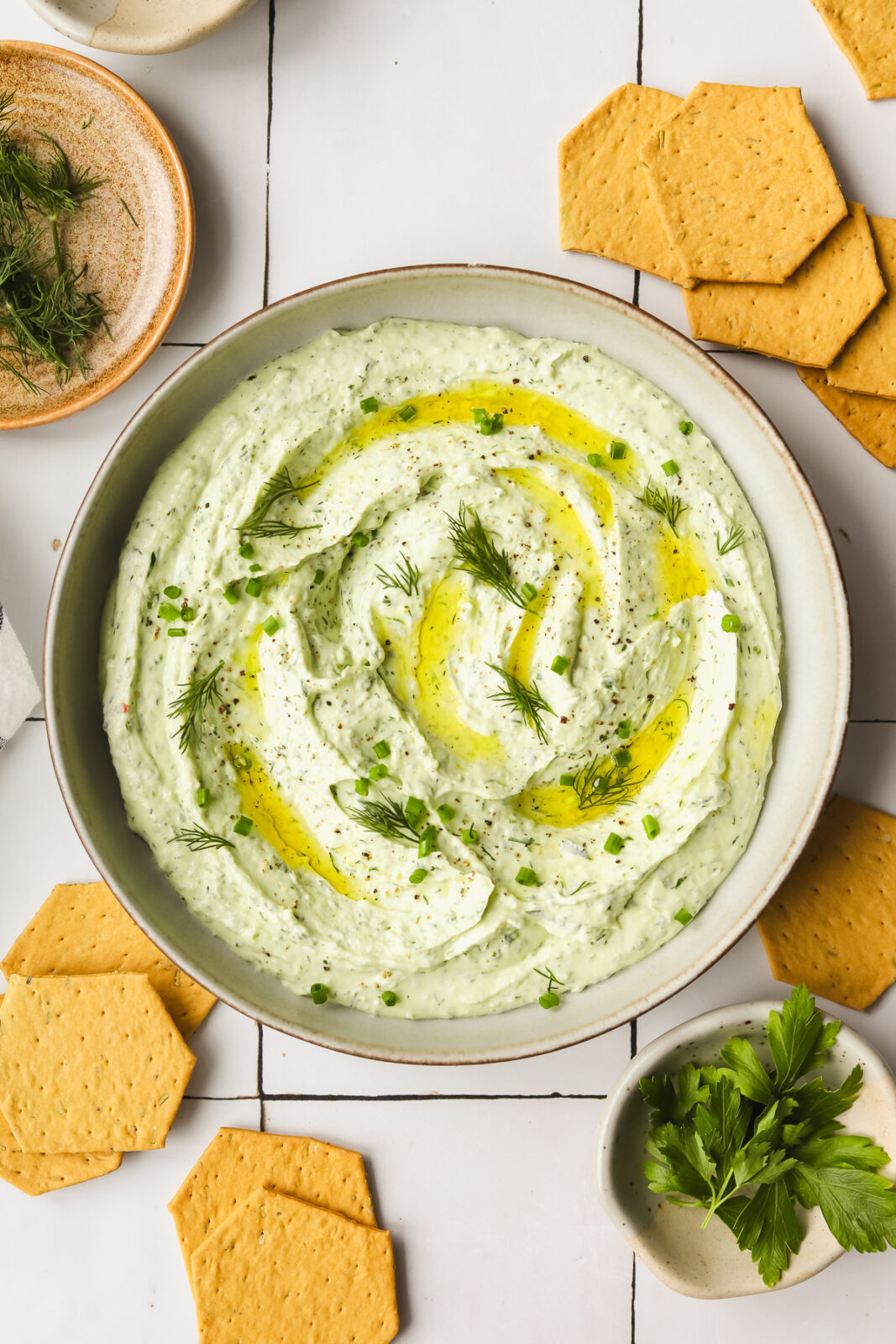 herby goat cheese spread in a shallow bowl with crackers and fresh herbs