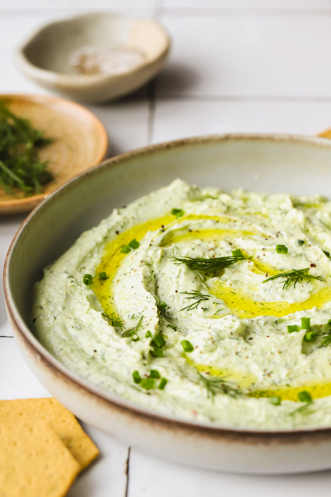 angled shot of a shallow bowl with herby goat cheese and olive oil drizzle