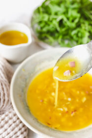 lemon shallot vinaigrette on a spoon being drizzled in to a bowl