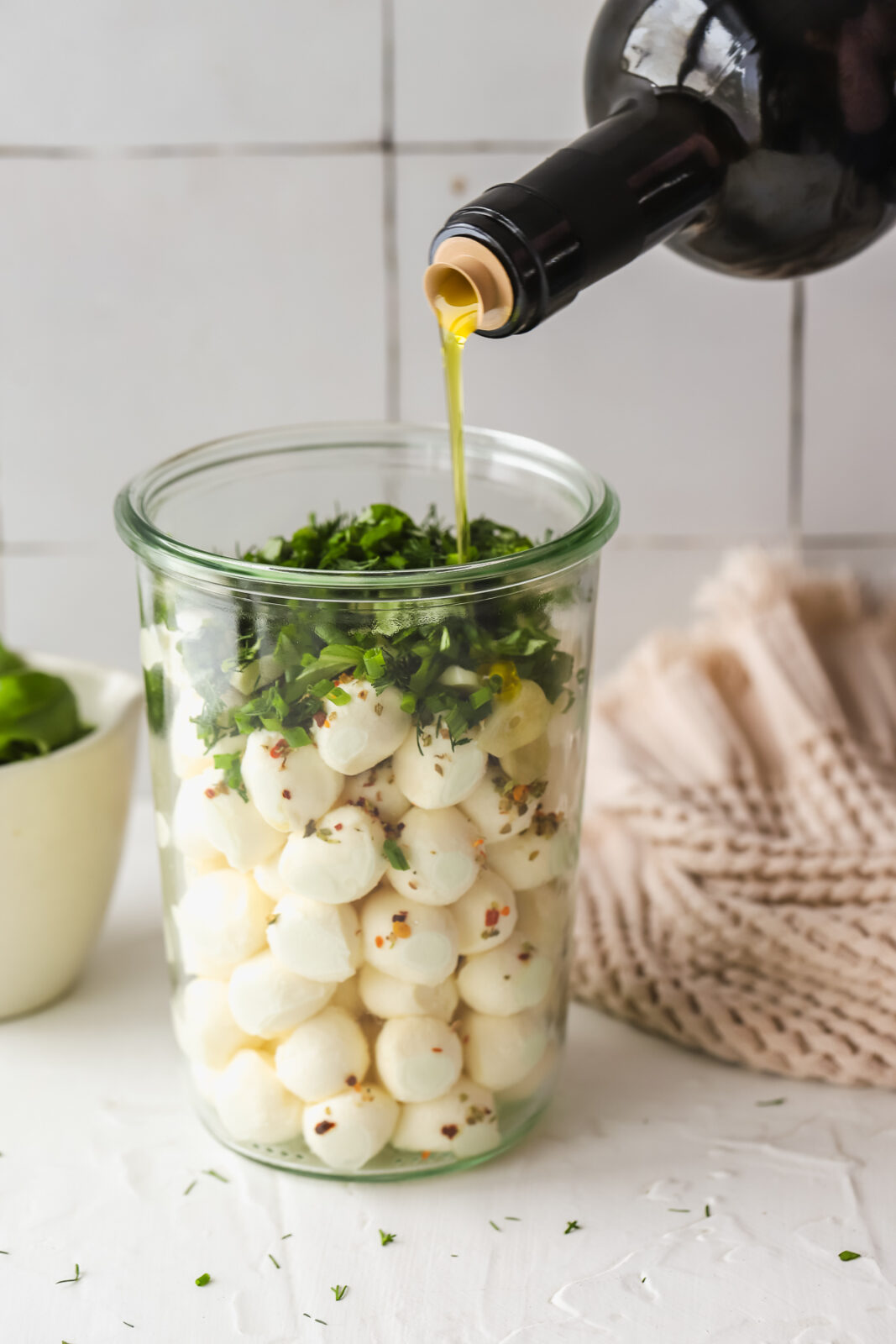 olive oil being poured into a jar with mozzarella balls