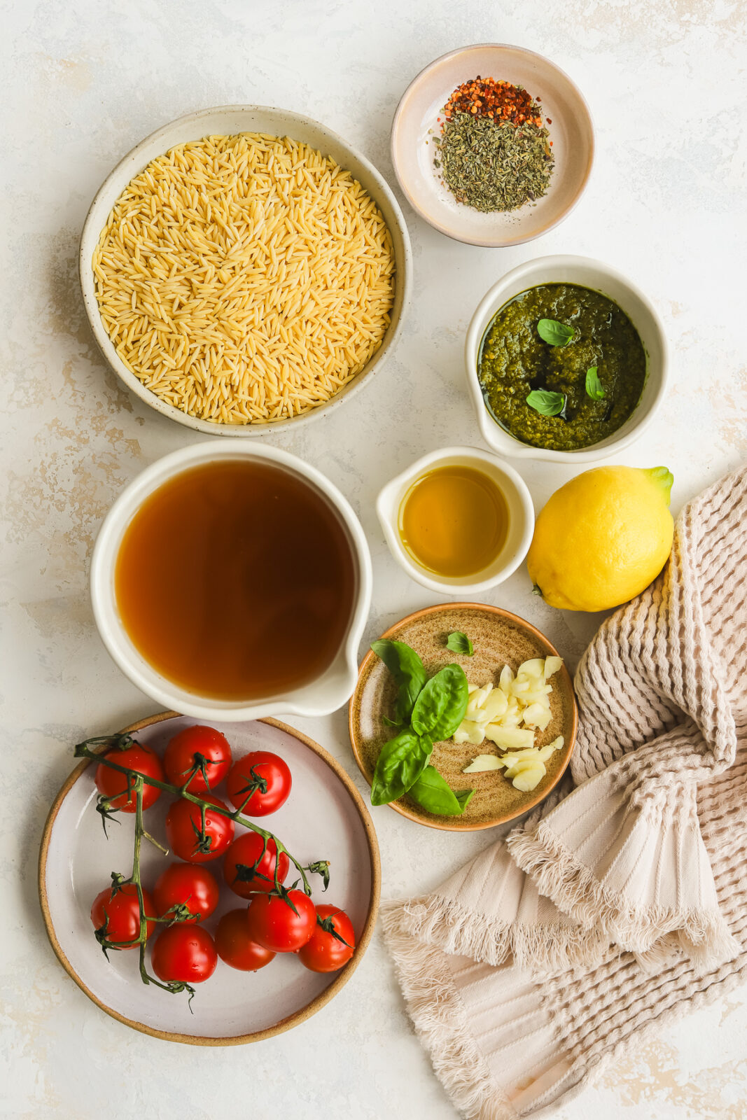 orzo in a bowl, vegetable broth in a bowl, fresh tomatoes on a plate, pesto in a bowl