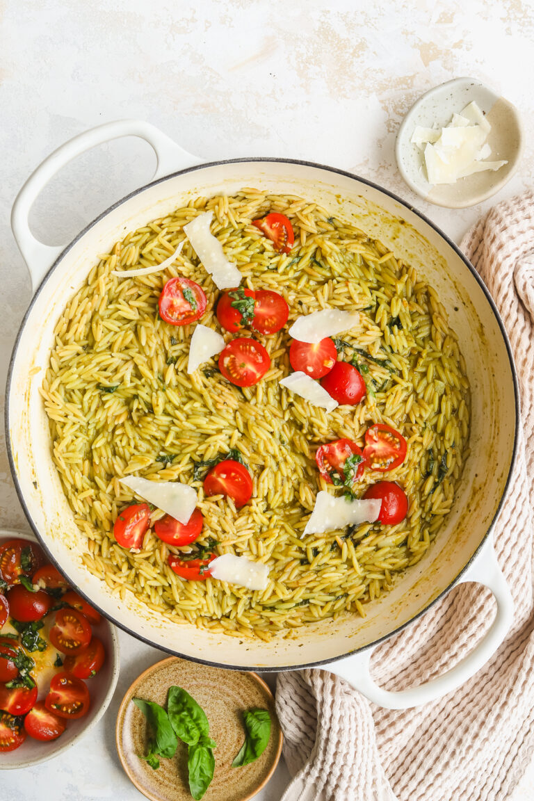 pesto orzo in a braiser topped with parmesan cheese and fresh tomatoes