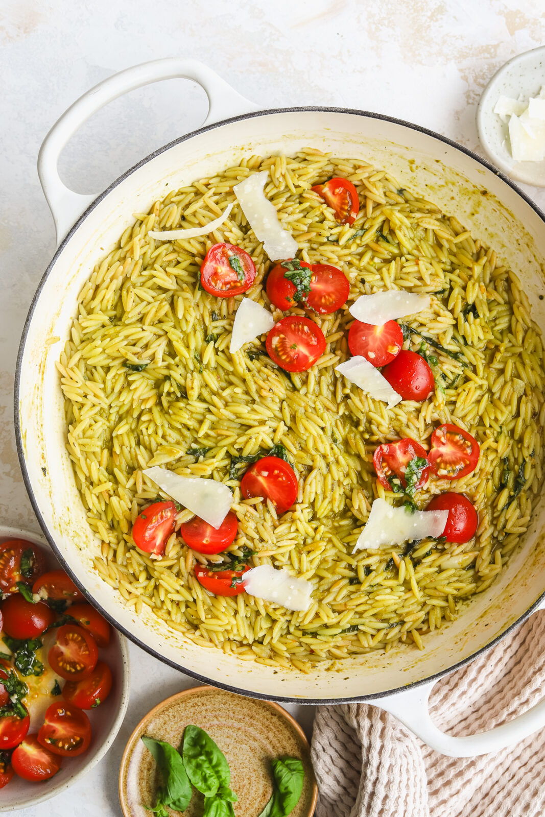 pesto orzo in a braiser topped with parmesan cheese and fresh tomatoes
