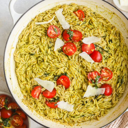 pesto orzo in a braiser topped with parmesan cheese and fresh tomatoes