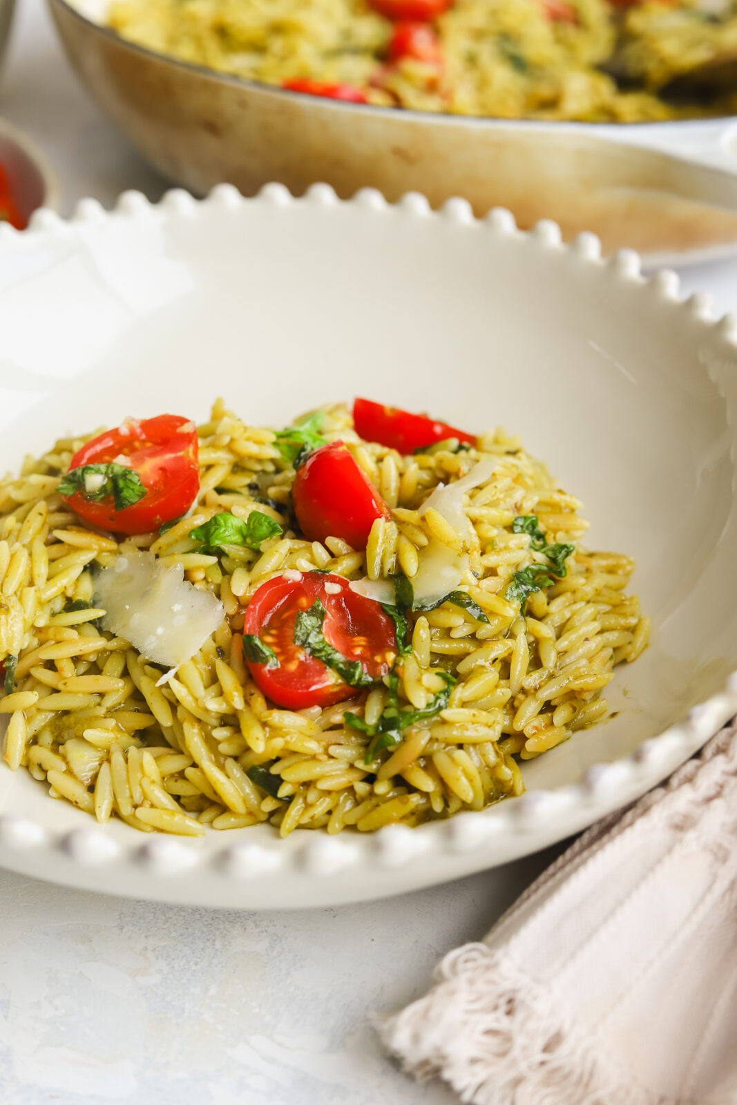 pesto orzo with tomatoes in a beige bowl