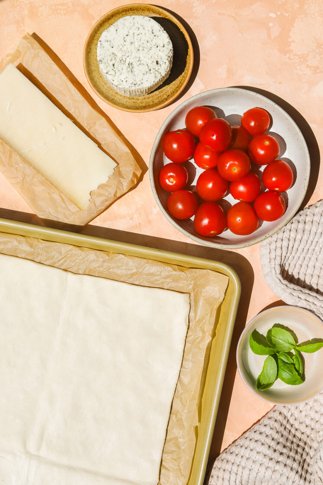 puff pastry on a baking sheet, tomatoes in a bowl, cheese on parchment paper