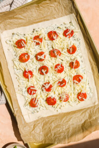 a sheet of puff pastry on a baking sheet topped with cheese and tomatoes
