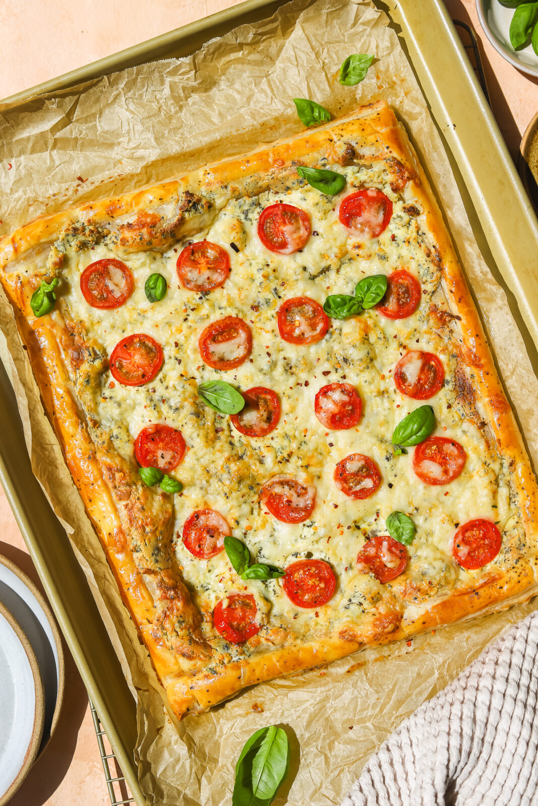 a baking sheet with a cooked tomato and cheese puff pastry tart