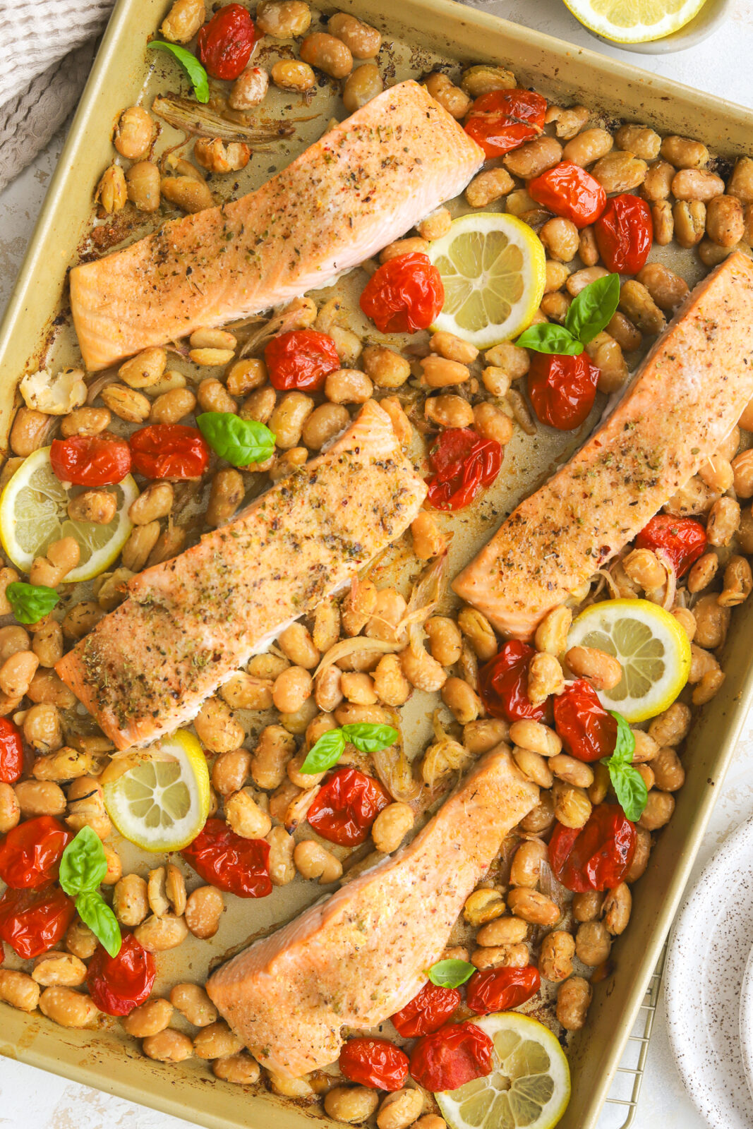 a sheet pan with burst tomatoes, butter beans and salmon fillets
