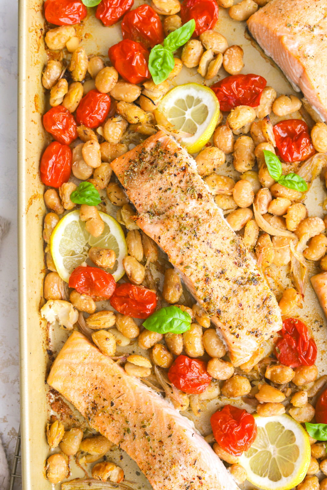 close up of a sheet pan with burst tomatoes, butter beans and salmon fillets