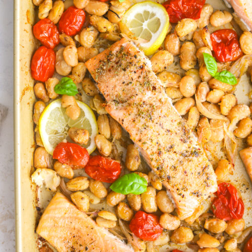 close up of a sheet pan with burst tomatoes, butter beans and salmon fillets