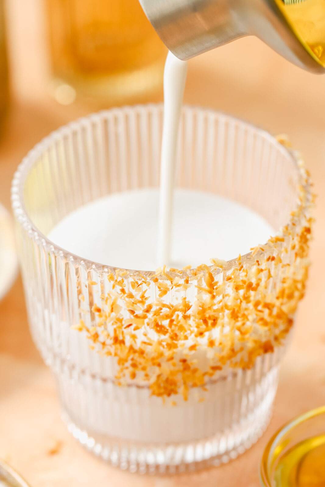 cocktail shaker pouring coconut margarita into a glass