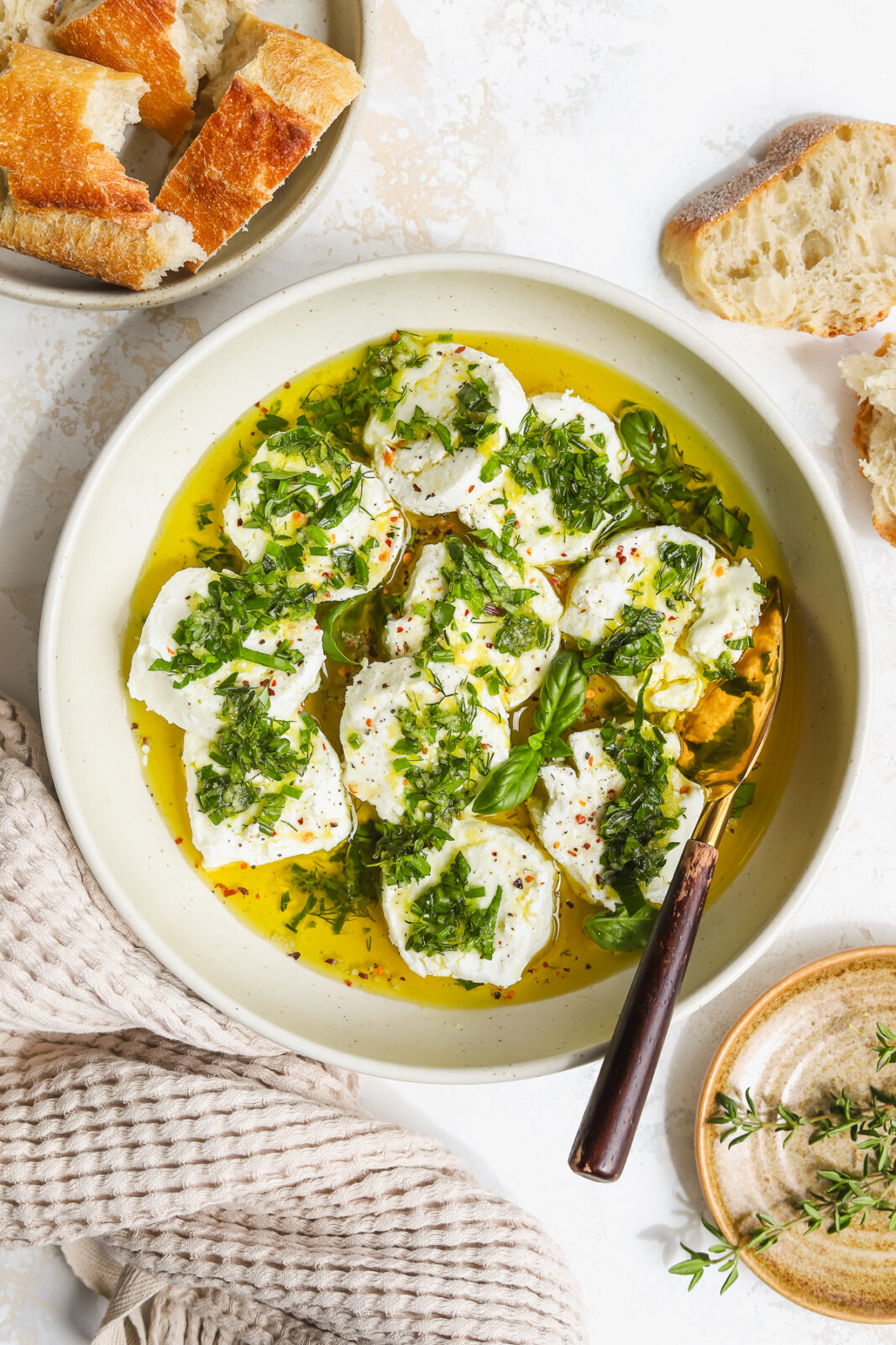 goat cheese marinated with fresh herbs, lemon, olive oil and garlic in a bowl with a serving knife