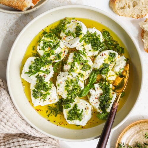 goat cheese marinated with fresh herbs, lemon, olive oil and garlic in a bowl with a serving knife